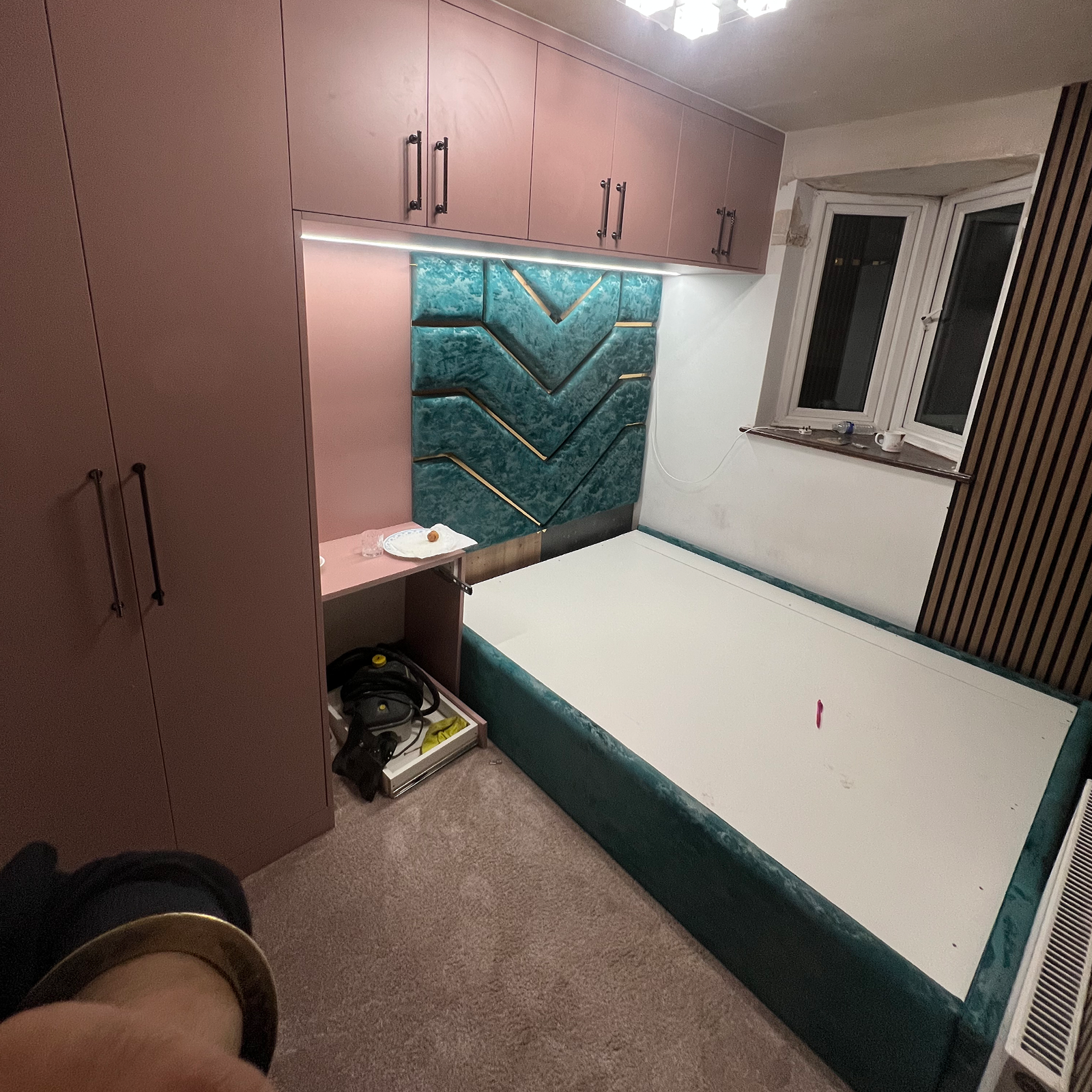 Stylish bedroom with teal upholstered bed and bespoke pink cabinetry